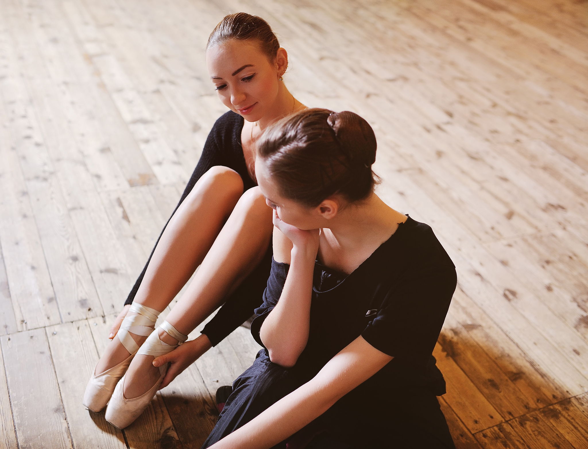 two ballerinas talking and smiling sitting on a wooden floor