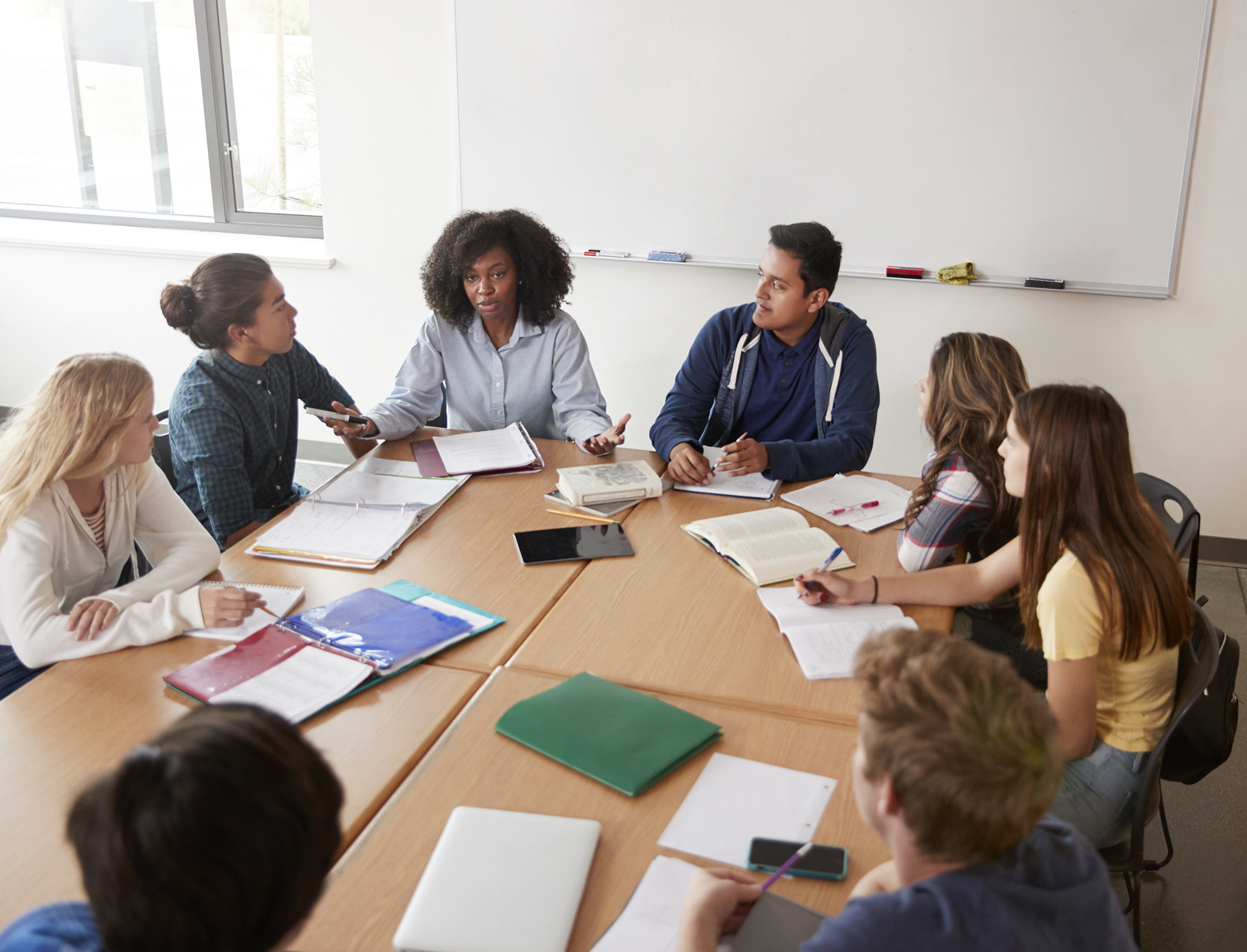 Female High School Tutor Sitting At Table With Pupils Teaching Maths Class