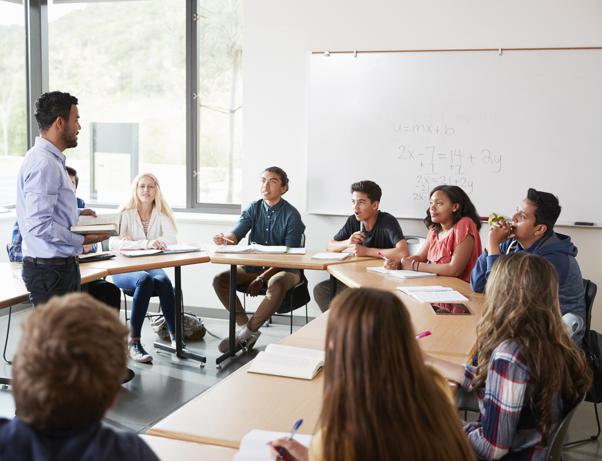 Male High School Tutor With Pupils Sitting At Table Teaching Maths Class